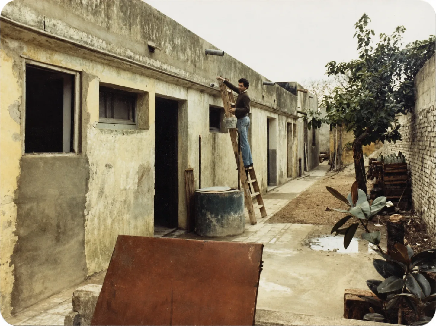 Casa y patio antiguos en obra, con una persona subida a una escalera trabajando en el acondicionamiento de la sede.